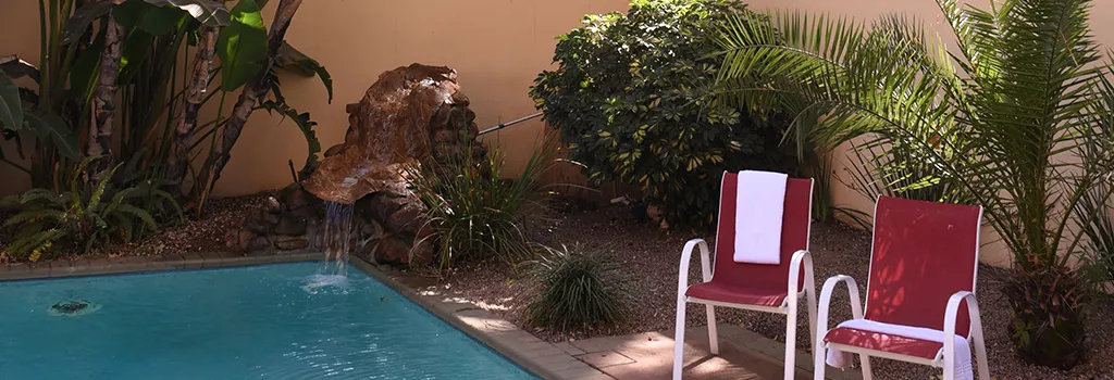 Two red chairs by a pool with a rock waterfall and lush greenery
