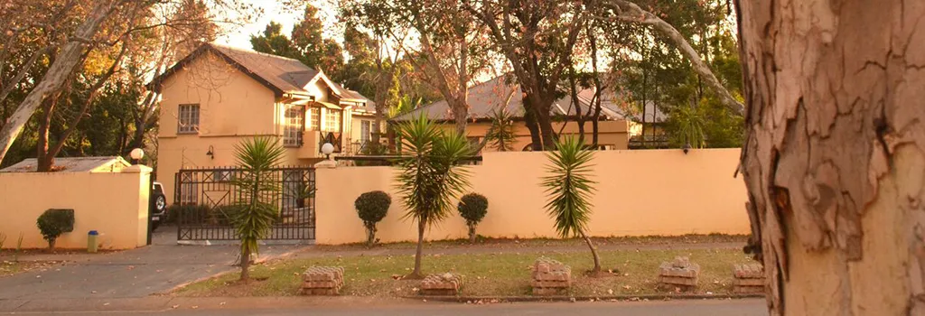 House with a gated entrance palm trees and a beige wall in a suburban setting