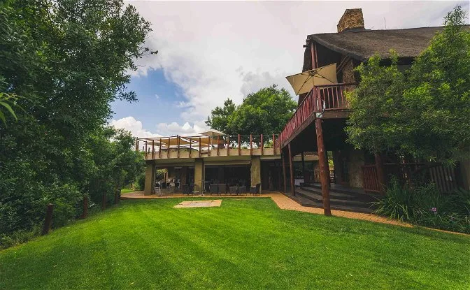 Large house with wooden deck and green lawn surrounded by trees