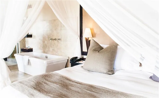Bedroom with canopy bed pillows and an adjacent bathtub with white curtains