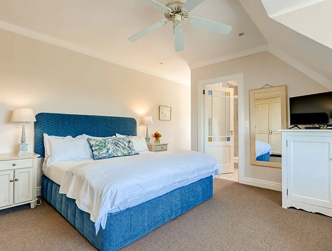 Blue upholstered bed in a cozy bedroom with a ceiling fan and mirror