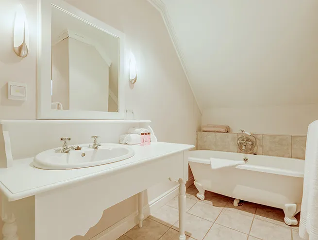 White bathroom with sink mirror and clawfoot bathtub under slanted ceiling