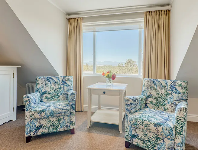 Two floral armchairs by a window with a view of trees and mountains