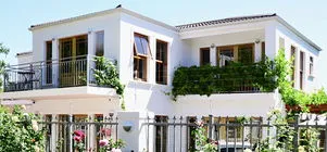White twostory house with balconies and metal fence surrounded by greenery