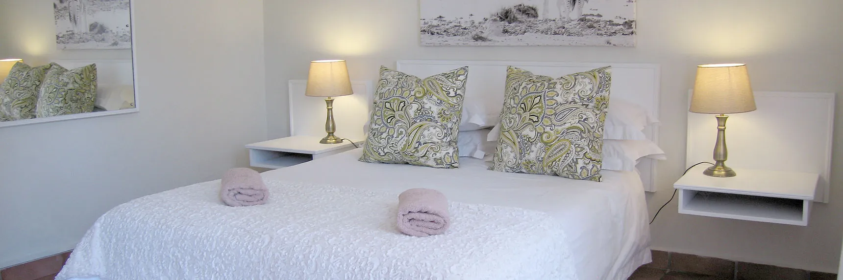 Neatly made bed with patterned pillows bedside tables and lamps in a bedroom