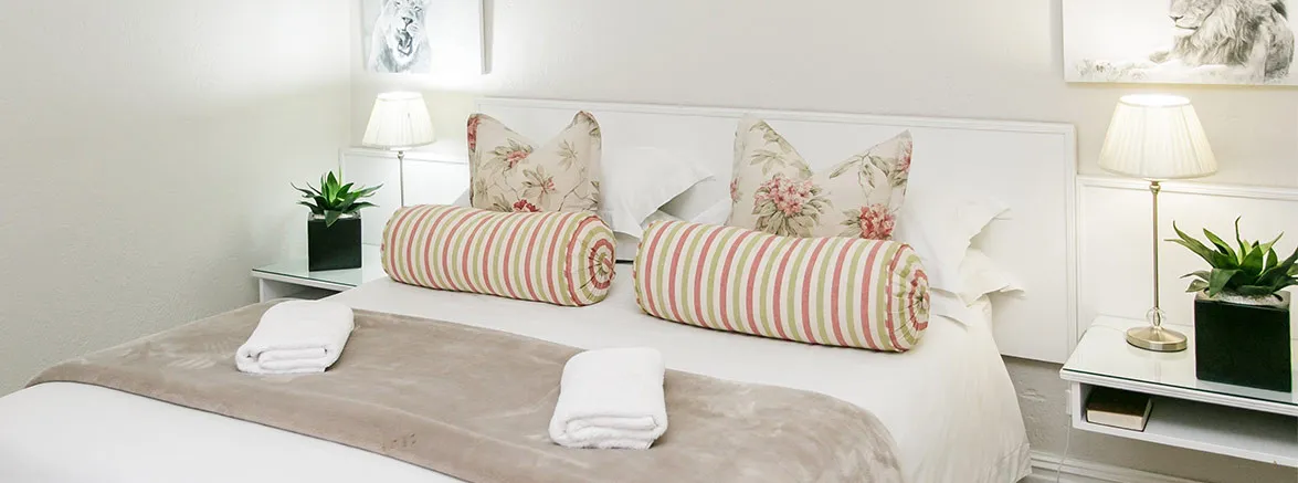 Neatly made bed with white linens striped bolsters and bedside lamps with plants