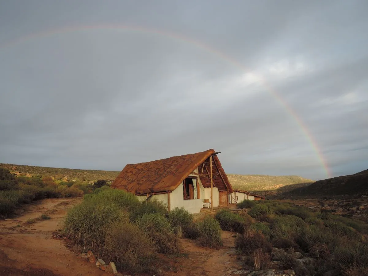 A rustic house with a rainbow in the background over a hilly landscape