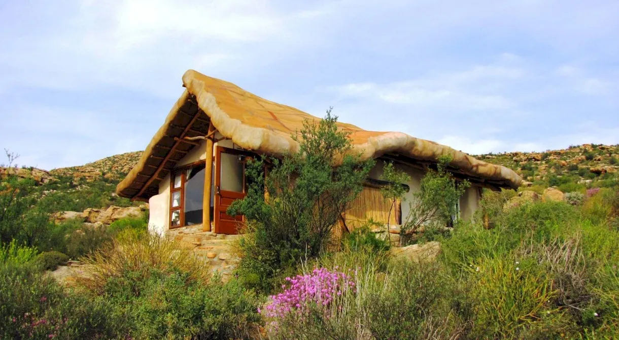 A thatchedroof cottage surrounded by greenery and hills in the background