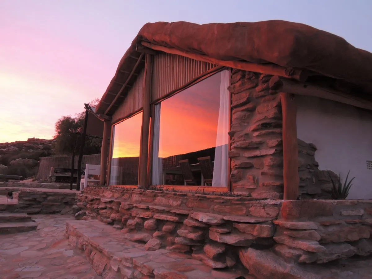 Stone building with large windows at sunset reflecting the sky