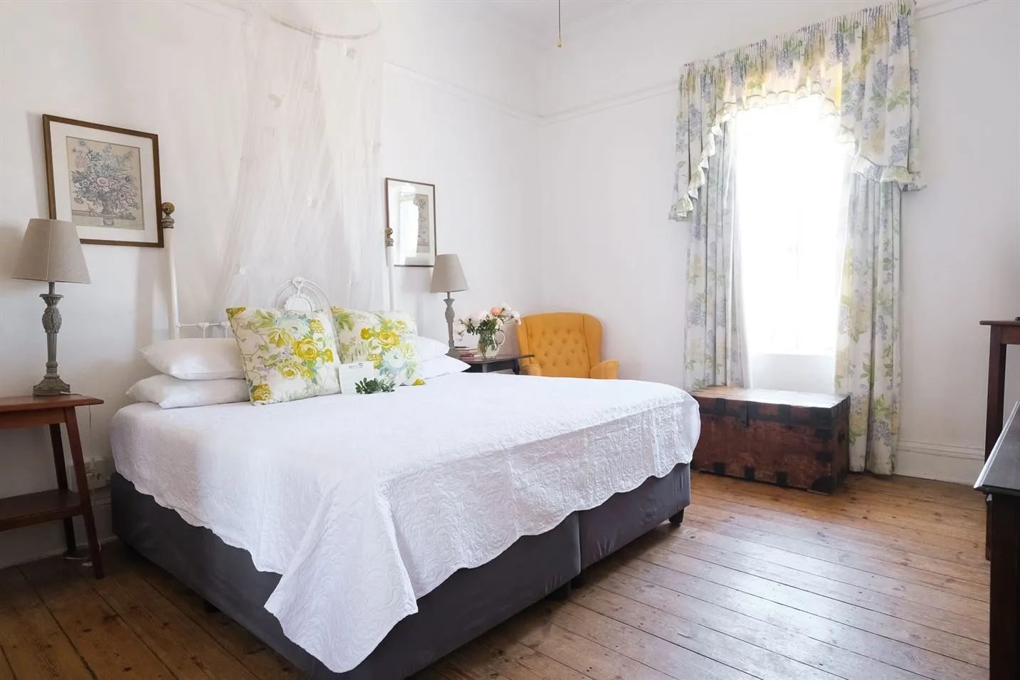 Bright bedroom with a large bed floral pillows and wooden floor