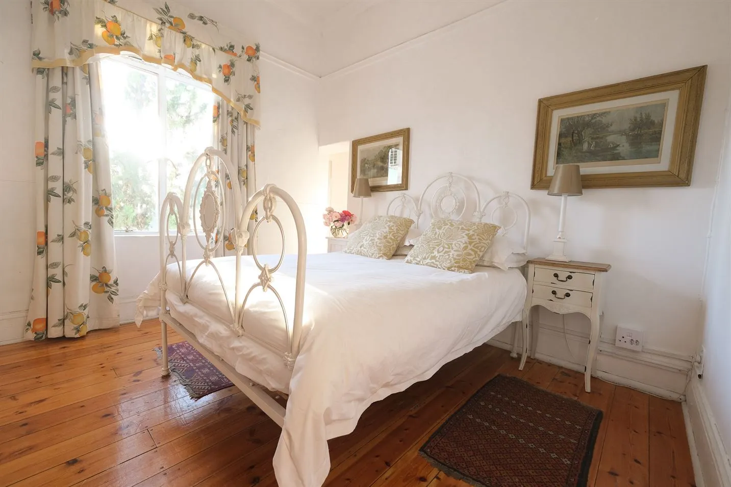 Bright bedroom with white iron bed floral curtains and wooden floor