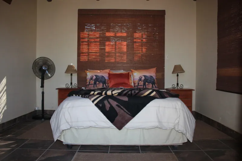 Bedroom with a bed elephant pillows and a fan in front of a window