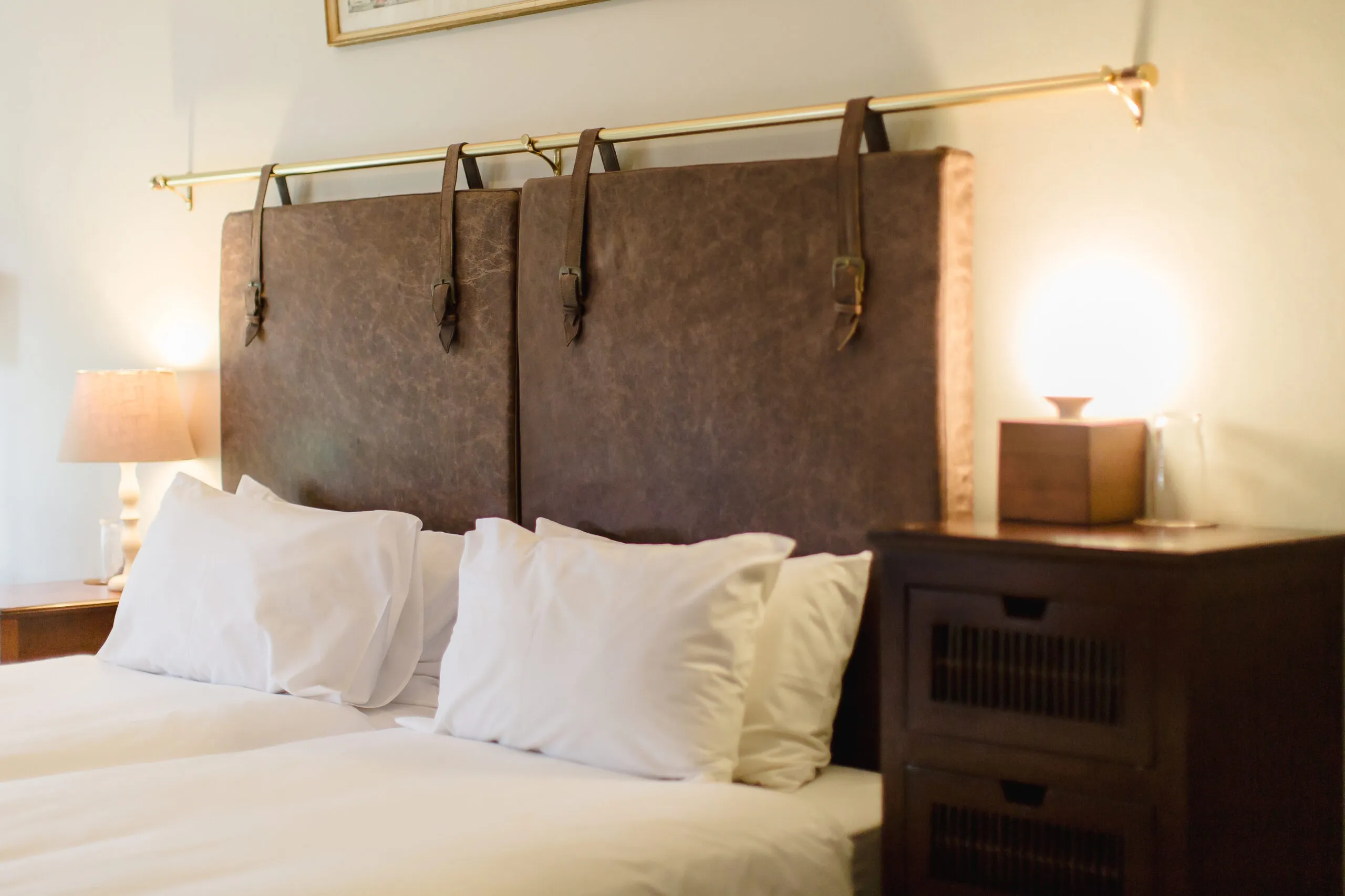 Brown upholstered headboard with pillows on a bed and bedside table with lamp