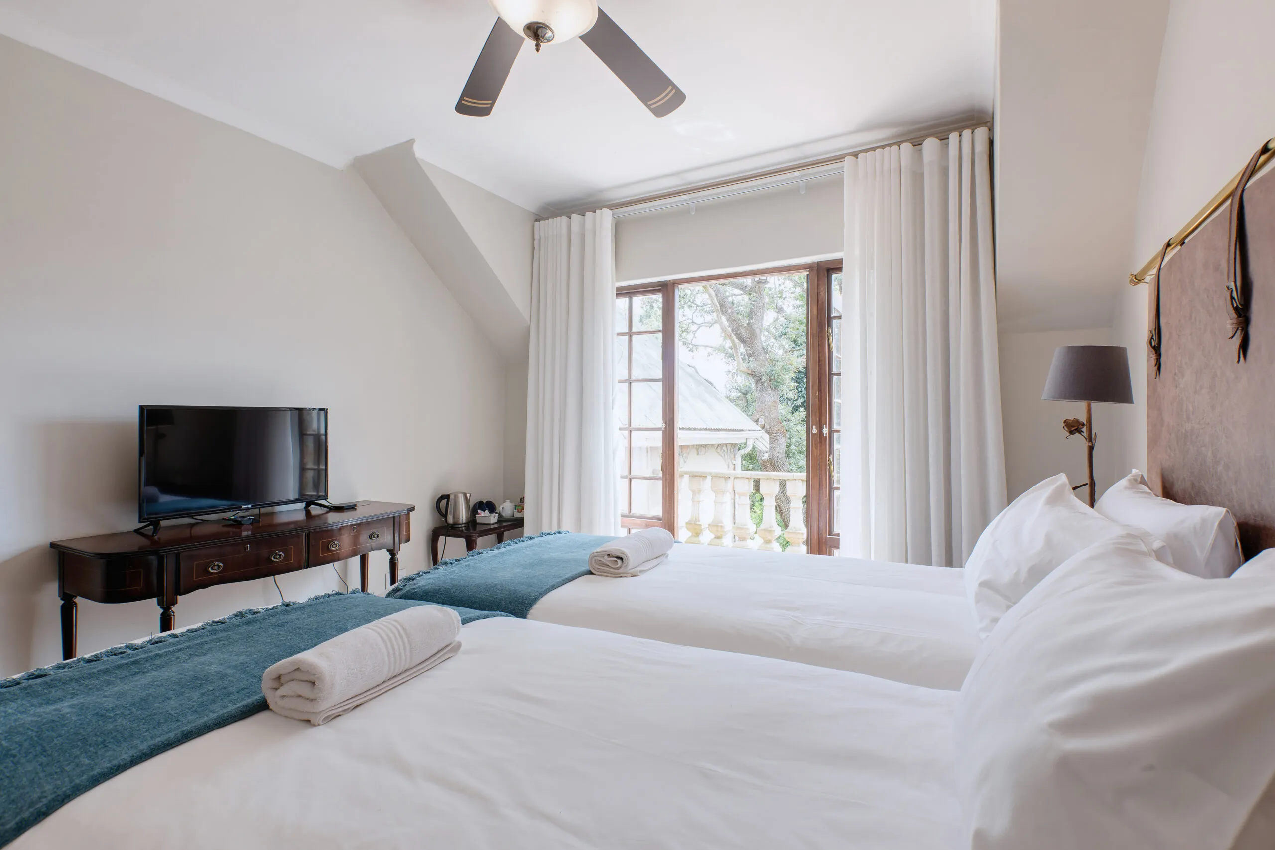 Two beds in a bright bedroom with a TV and large window