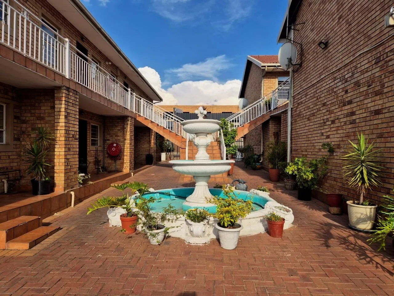 Courtyard with a tiered fountain potted plants and brick buildings on either side