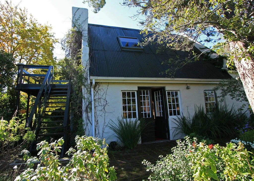 Cottage with a black roof surrounded by greenery and a staircase on the left