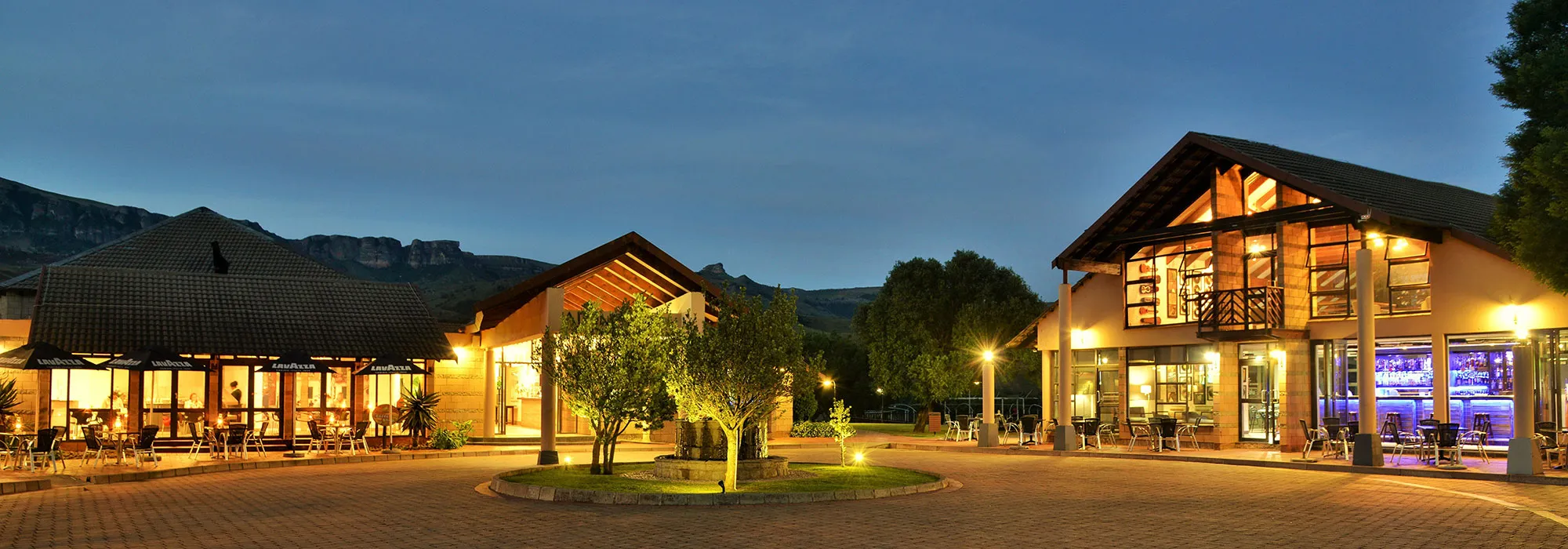 Evening view of a warmly lit resort with dining areas and trees