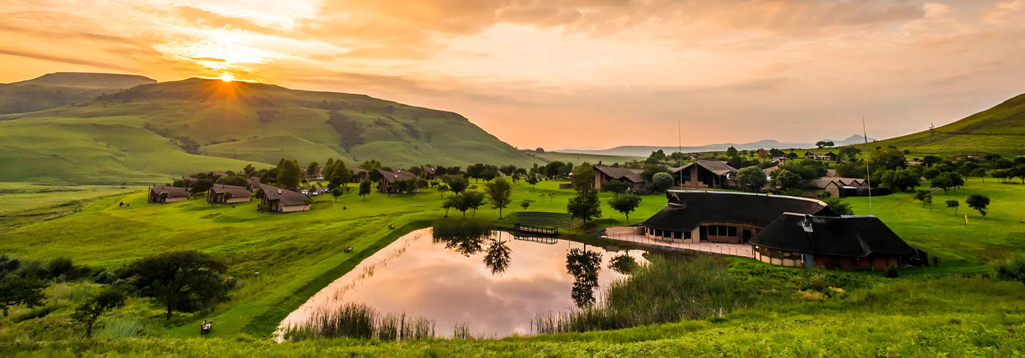 Sunset over a serene countryside with buildings and a reflective pond