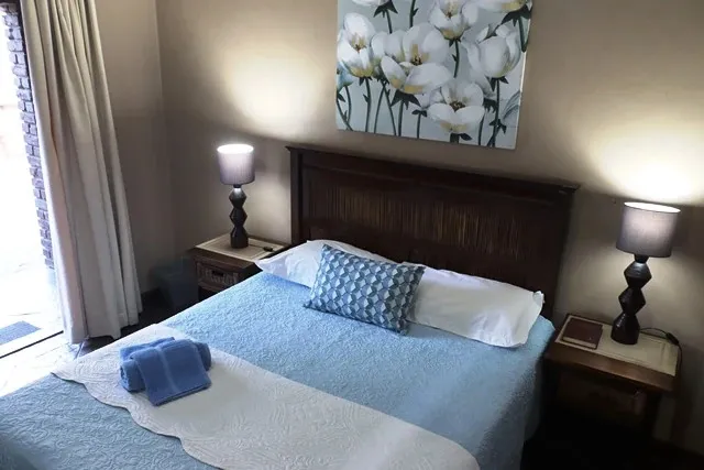 A neatly made bed in a bedroom with floral wall art and bedside lamps