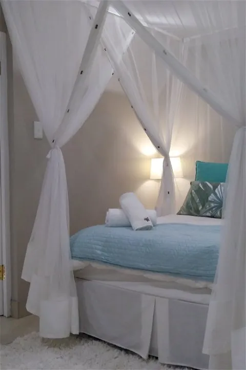 White canopy bed with blue blanket and pillows in a cozy bedroom