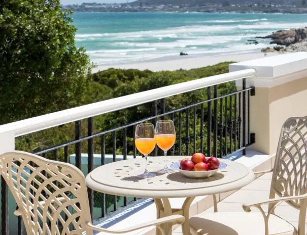 Two drinks and fruit on a table with ocean view from a balcony