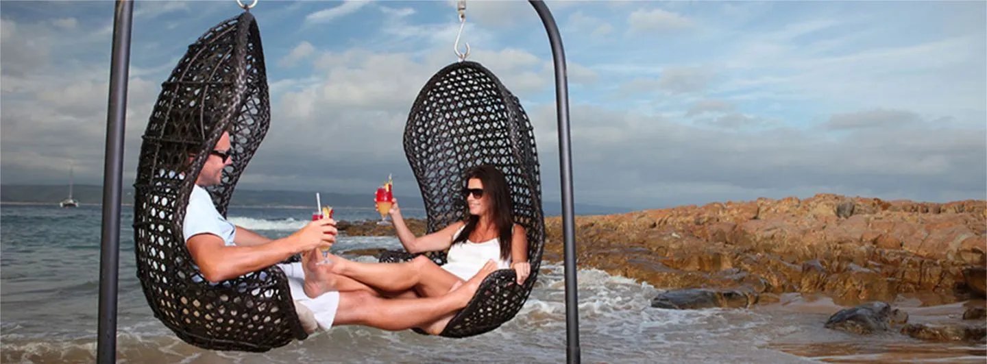 Couple relaxing in hanging chairs by the ocean holding drinks