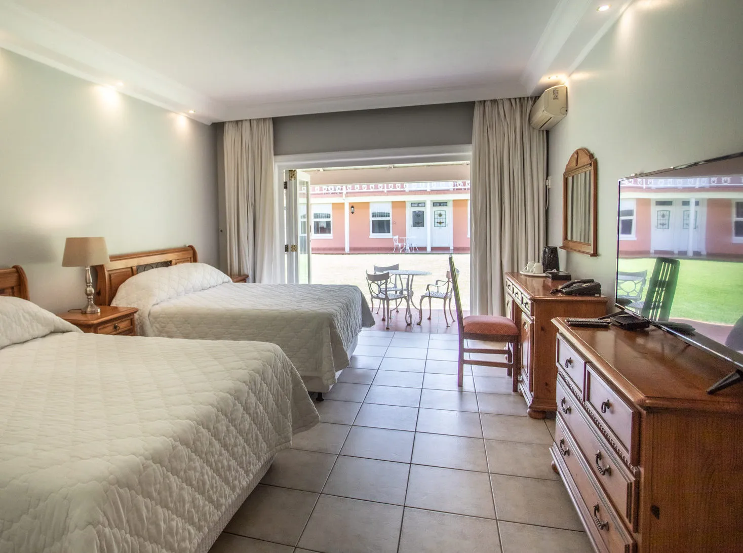 Hotel room with two beds wooden furniture and a view of a courtyard