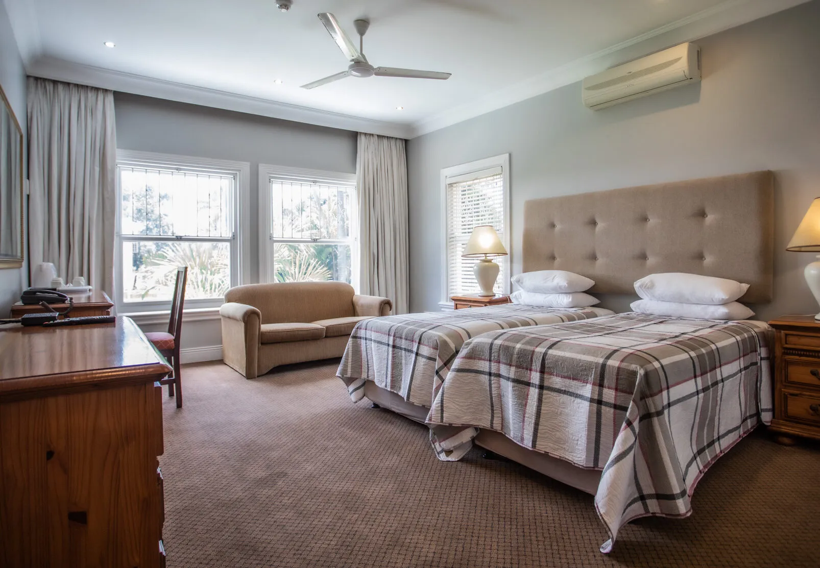 Bedroom with two beds sofa desk and large windows with curtains