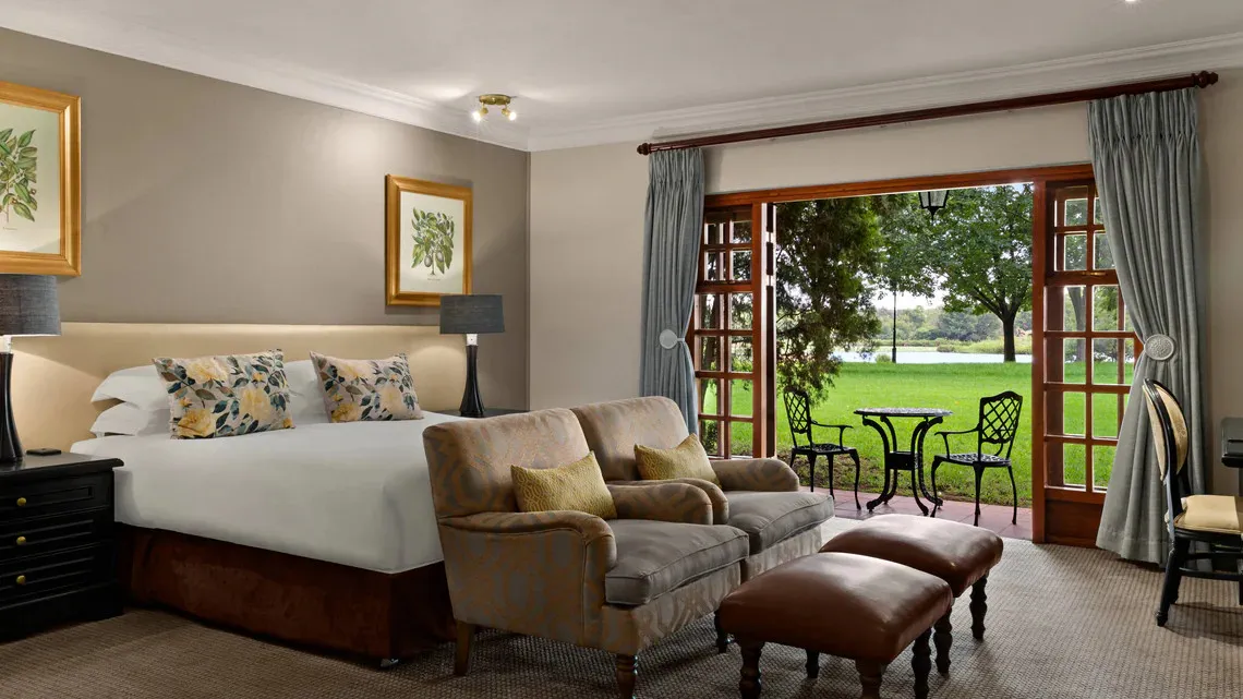 Bedroom with large bed armchairs and open doors to a garden view