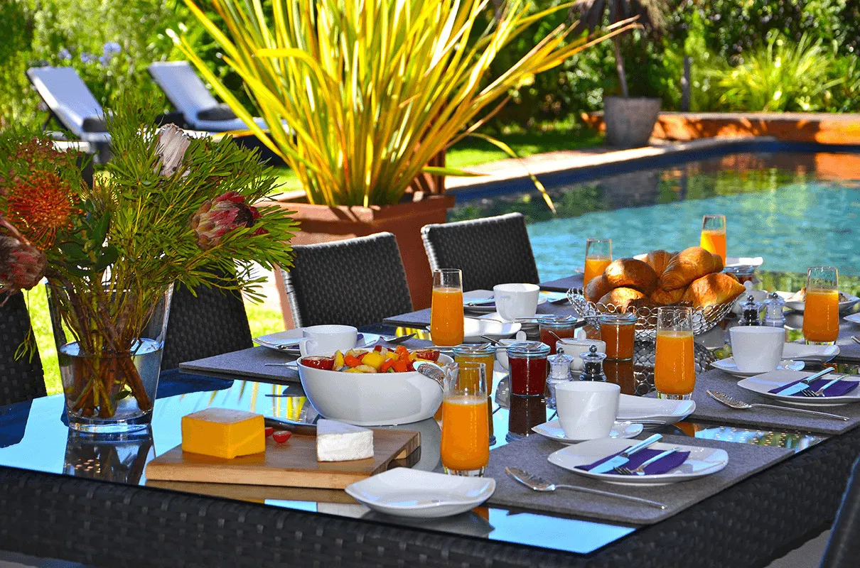 Outdoor breakfast setup by a pool with fruit juice and pastries