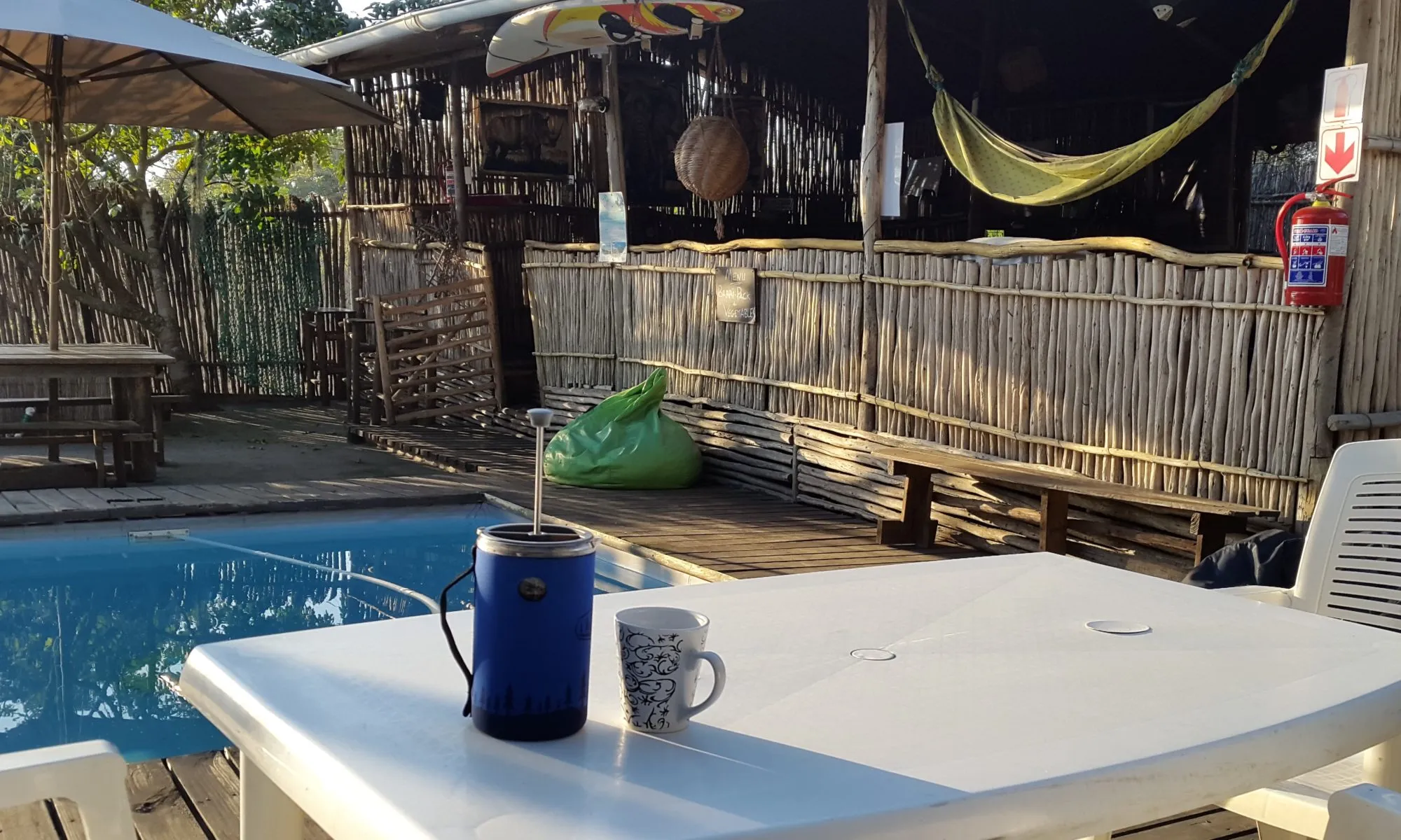 Coffee cup and thermos on table by pool in tropical setting