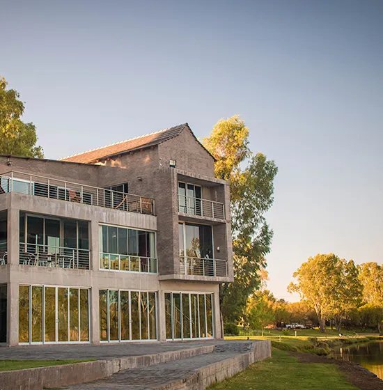 Modern house with large windows and balcony surrounded by trees and a pond