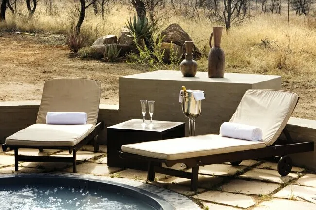 Two lounge chairs with towels by a table with wine glasses and vases outdoors