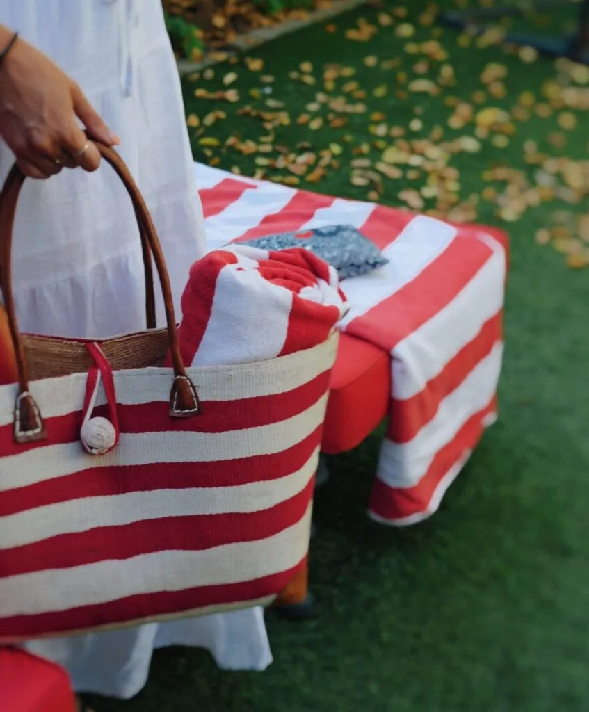 Hand holding a red and white striped bag in a garden setting