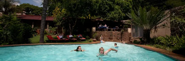 People swimming in a pool with a garden and lounge area in the background