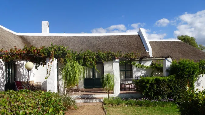 White cottage with thatched roof green plants and blue sky background