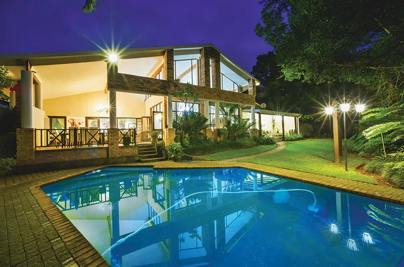 Modern house with pool at night surrounded by trees and lit by spotlights