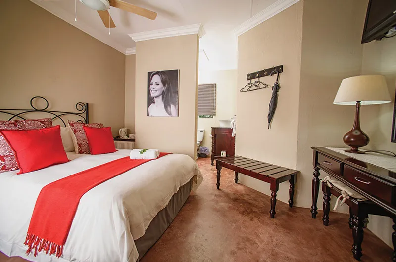 Bedroom with red and white bedding wooden furniture and a large portrait on the wall