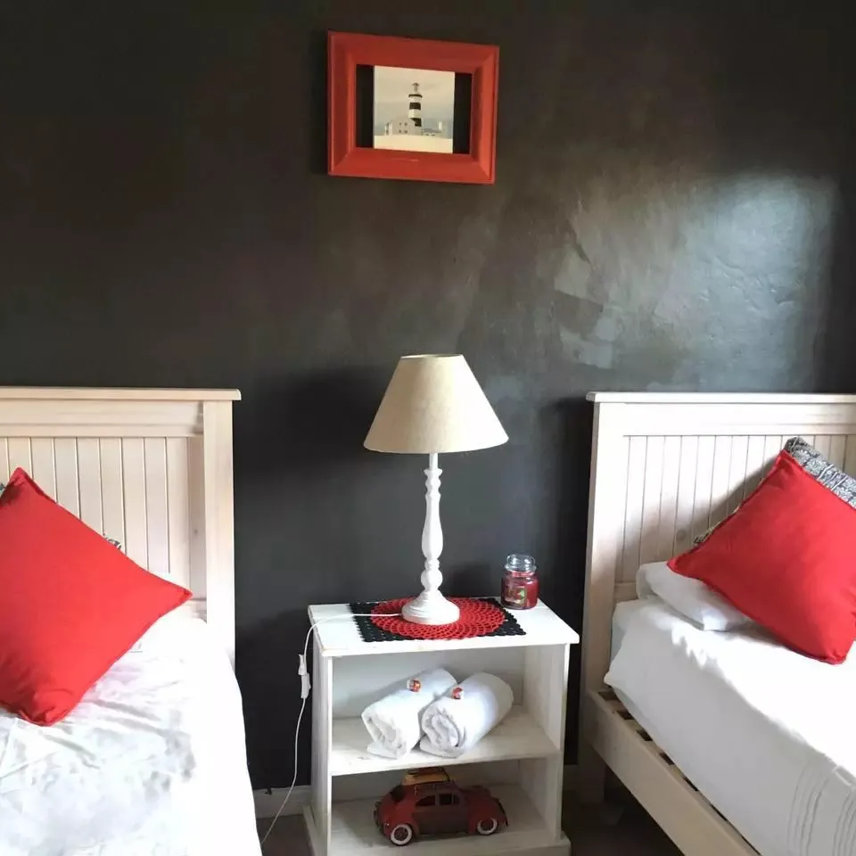 Two single beds with red pillows white lamp and red wall art
