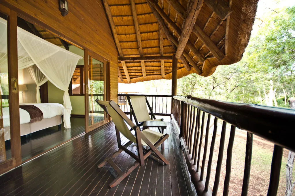 Wooden deck with lounge chairs overlooking a forest adjacent to a bedroom