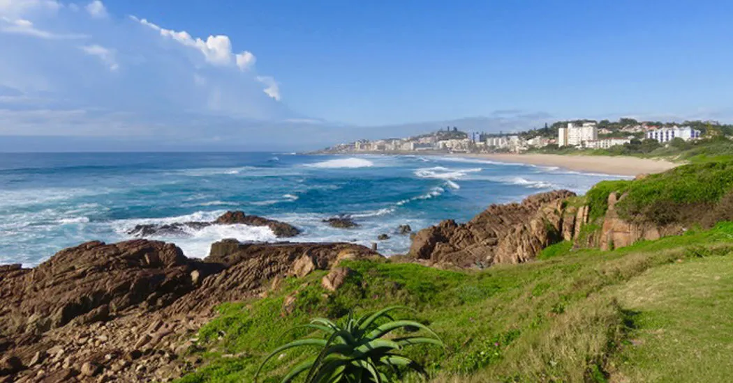 Rocky coastline with ocean waves and buildings in the background