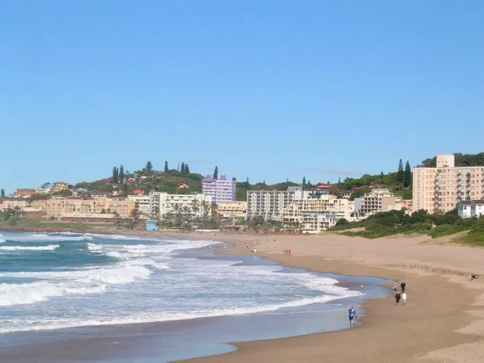 Beach with waves people walking and buildings on a hill in the background