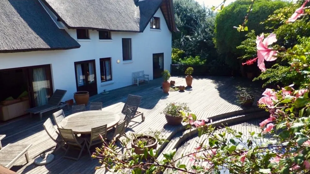 White house with wooden deck outdoor furniture and potted plants in sunny garden