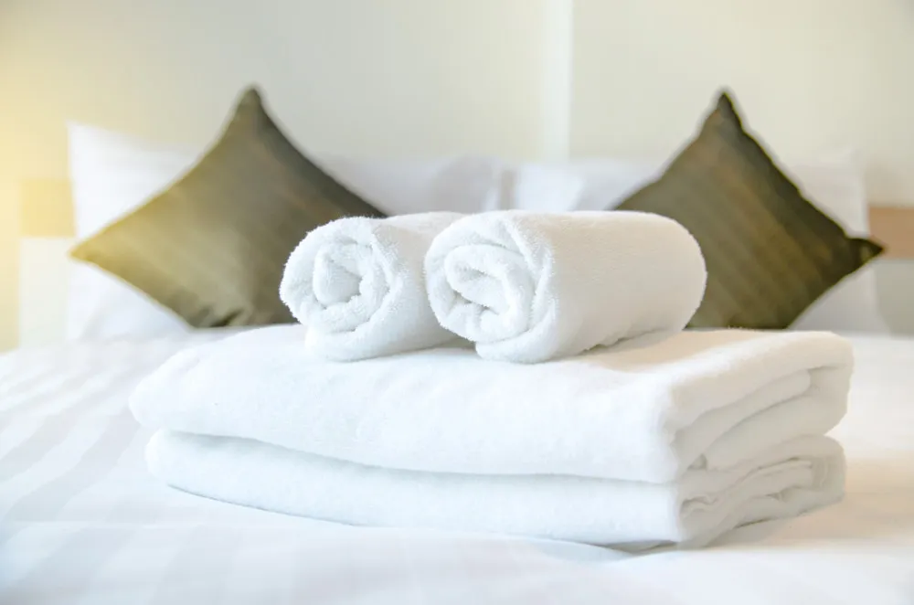 Two rolled towels on a stack of towels on a bed with pillows