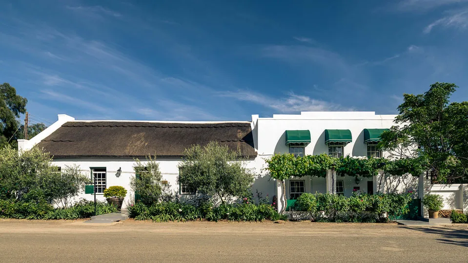 White building with green awnings thatched roof and lush greenery under blue sky