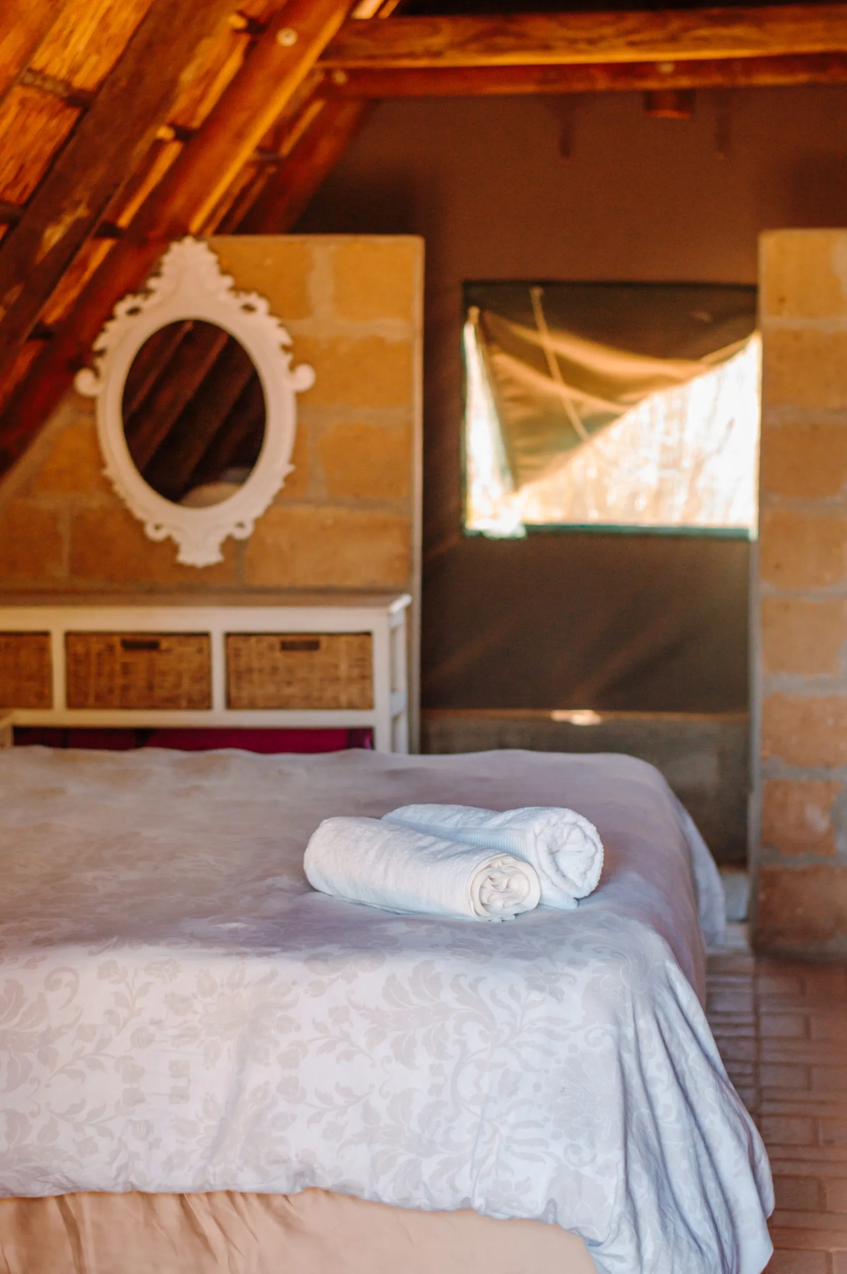 Bed with rolled towels in a rustic room with stone walls and wooden ceiling