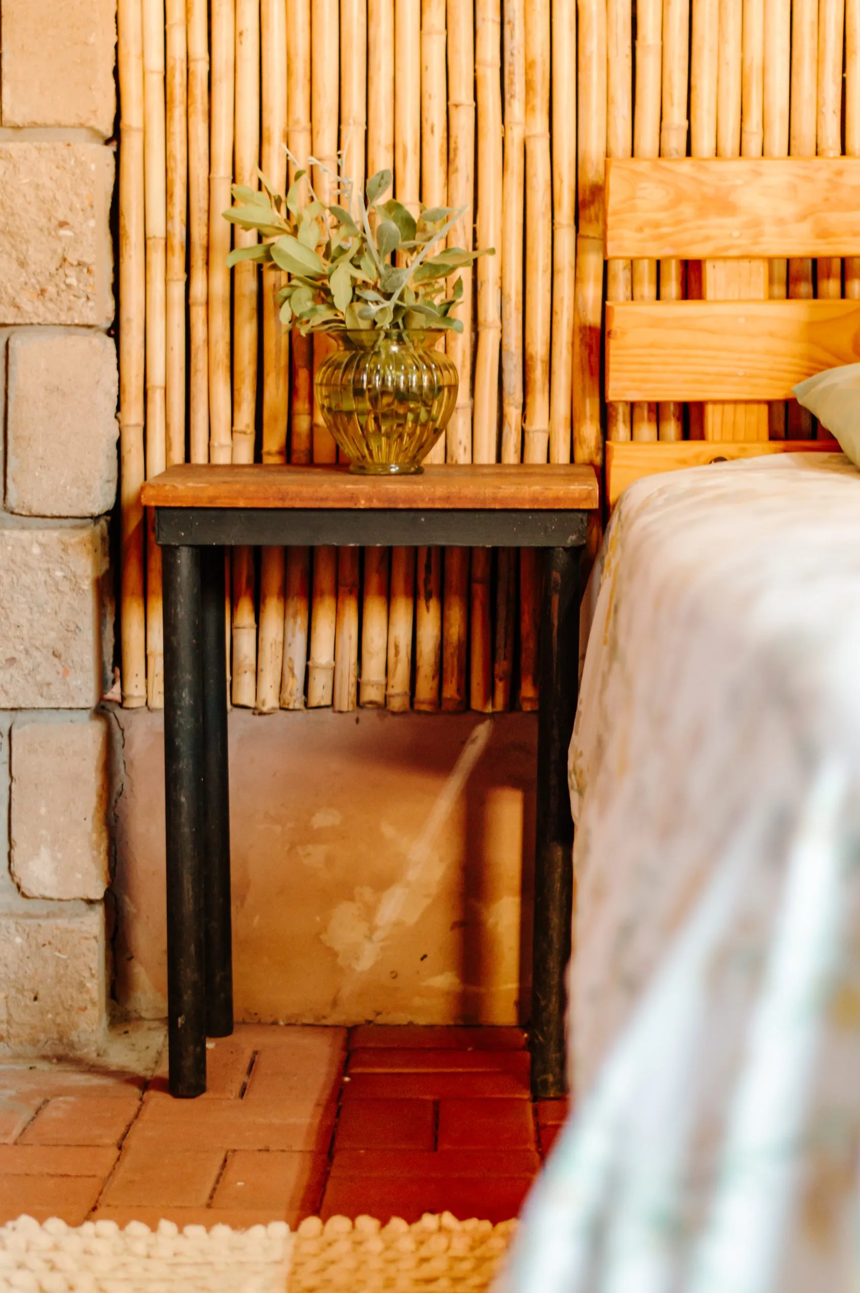 Wooden bed with a plant on a side table next to a bamboo wall