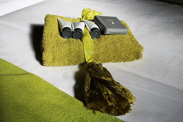 Folded yellow towel with toiletries and a tassel on a white surface