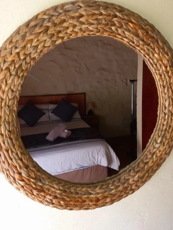 Woven circular mirror reflecting a bedroom with a bed and pillows