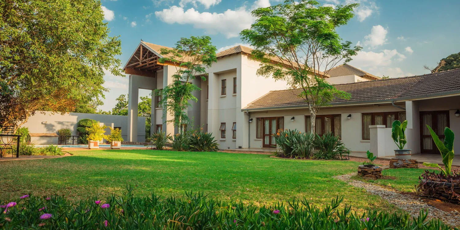 Modern house with large lawn trees and flowers under a blue sky